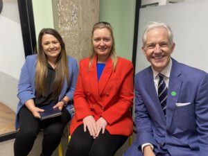 Two females and one male, sat down at a prize giving event, smiling for their photo.