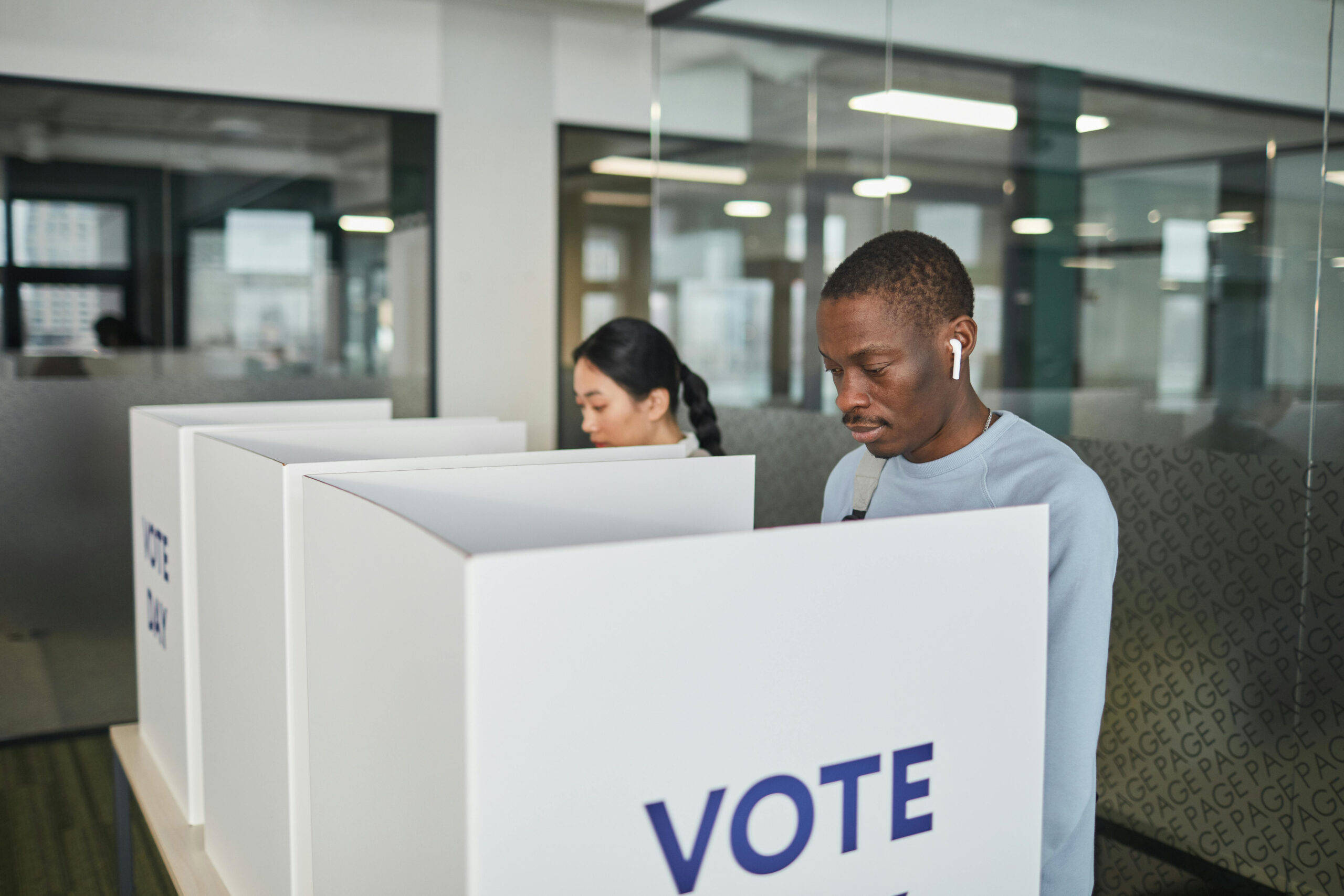 A young man and a young woman in voting booths about to cast their votes.