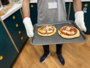 Close-up of two cooked pizza's in an oven tray held by a man wearing oven gloves.