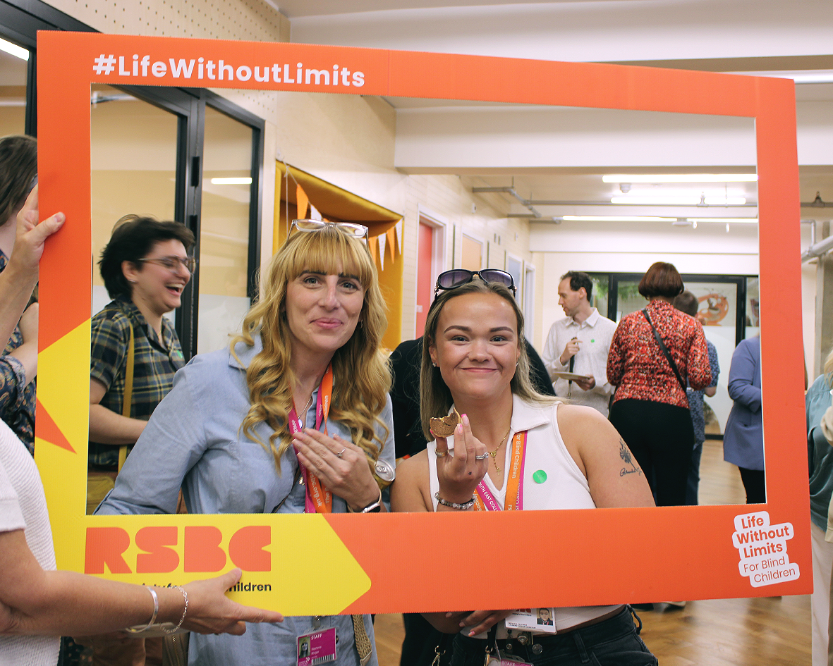 Two RSBC staff members posing together in big novelty selfie frame at an RSBC event. From left to right: a light-skinned woman with beautifully curled long blonde hair , she has a pair of glasses on her head, a light-skinned woman with straight medium blonde hair.