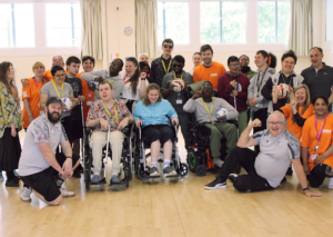 A group photo of the Dorton College students and staff at a sports activity day with Crystal Palace. There are approx. 30 people huddled into the shot. In the front row there are three students in wheelchairs, with the rest fo the group standing behind them. Everyone is smiling and cheering.