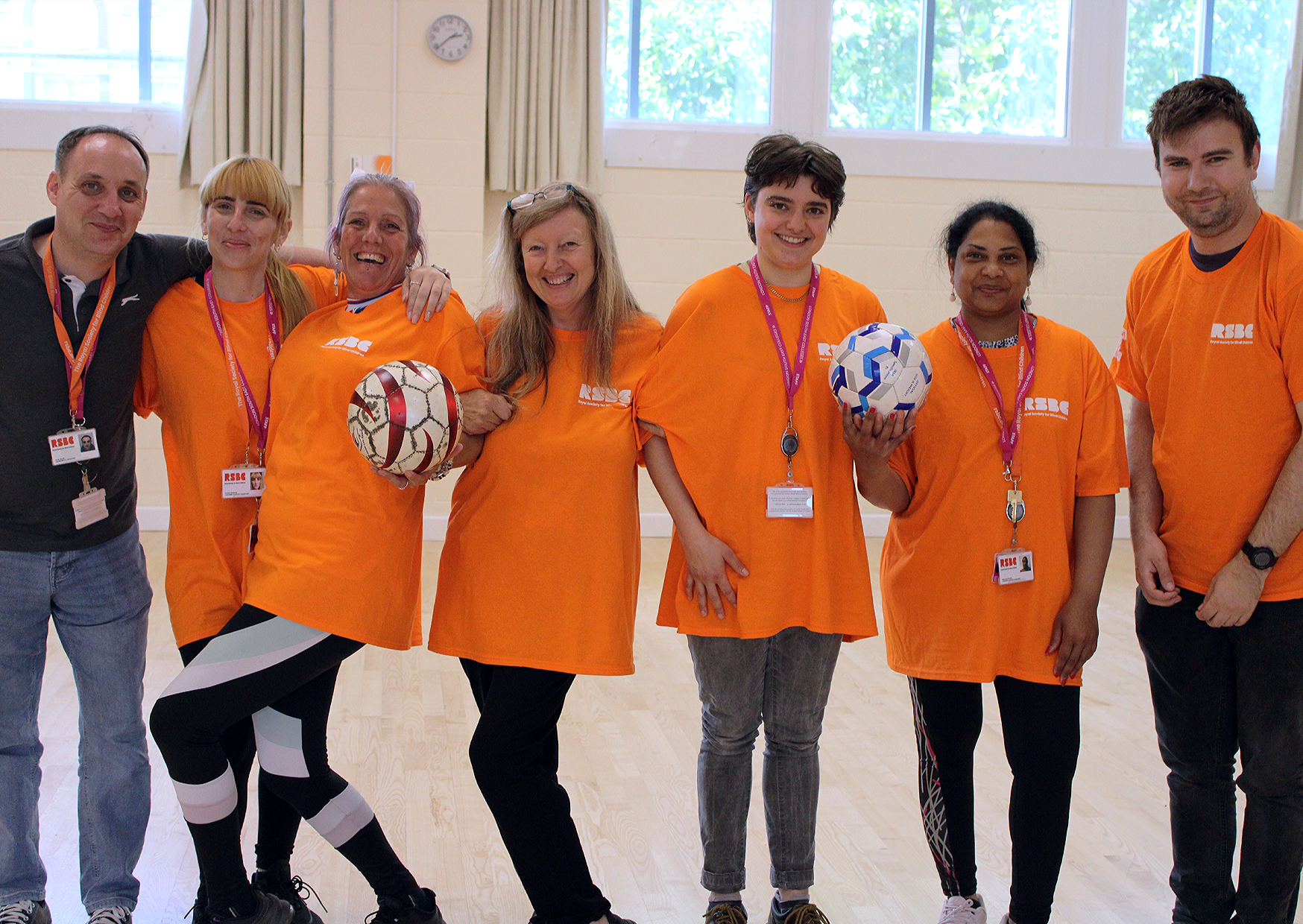 A group photo of seven Dorton College staff members. They are all huddled together smiling at the. They're all wearing bright orange RSBC t-shirts, except the person on the far left who didn't get the memo, wearing a navy t-shirt.