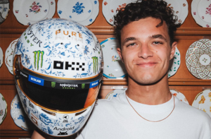 Lando Norris, a young Formula 1 driver in a porcelain store, holding up a hand-painted racing helmet, decorated in a vintage porcelain design.