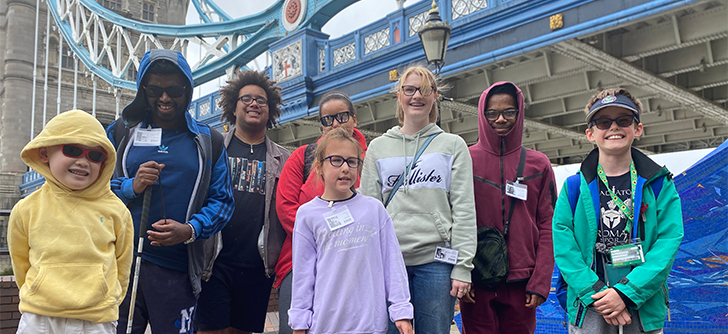 A group of young people standing on the bank of the Thames. Behind them is tower bridge.