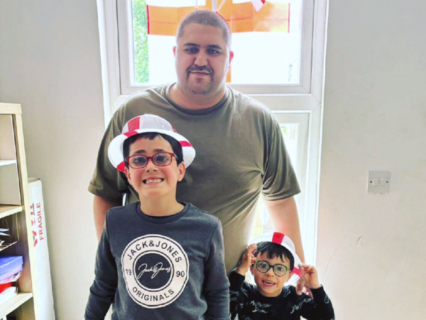 Dad Joe with his two boys Noah and Lyle. Joe is standing with the two young boys on either side of him. Joe is medium-light skinned and buzzed-short black hair. Noah aged 9, on the left, is medium-light skinned with red glasses. Lyle aged 3, on the right, medium-light skinned with blue glasses. All three are smiling at the camera brightly.