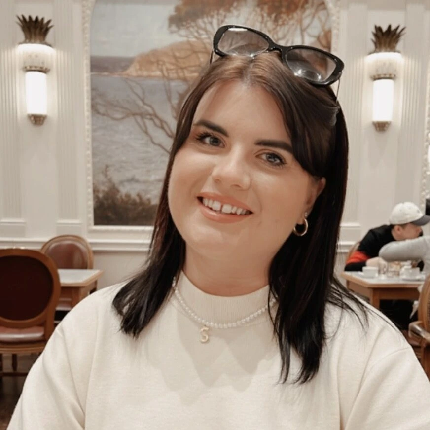 Headshot of Shannon, the Strategic Relationships Manager for RSBC. Shannon is a ligth-skinned woman with medium-length brown hair. She is wearing a white jumper with a pair of sunglasses perched on top of her head.