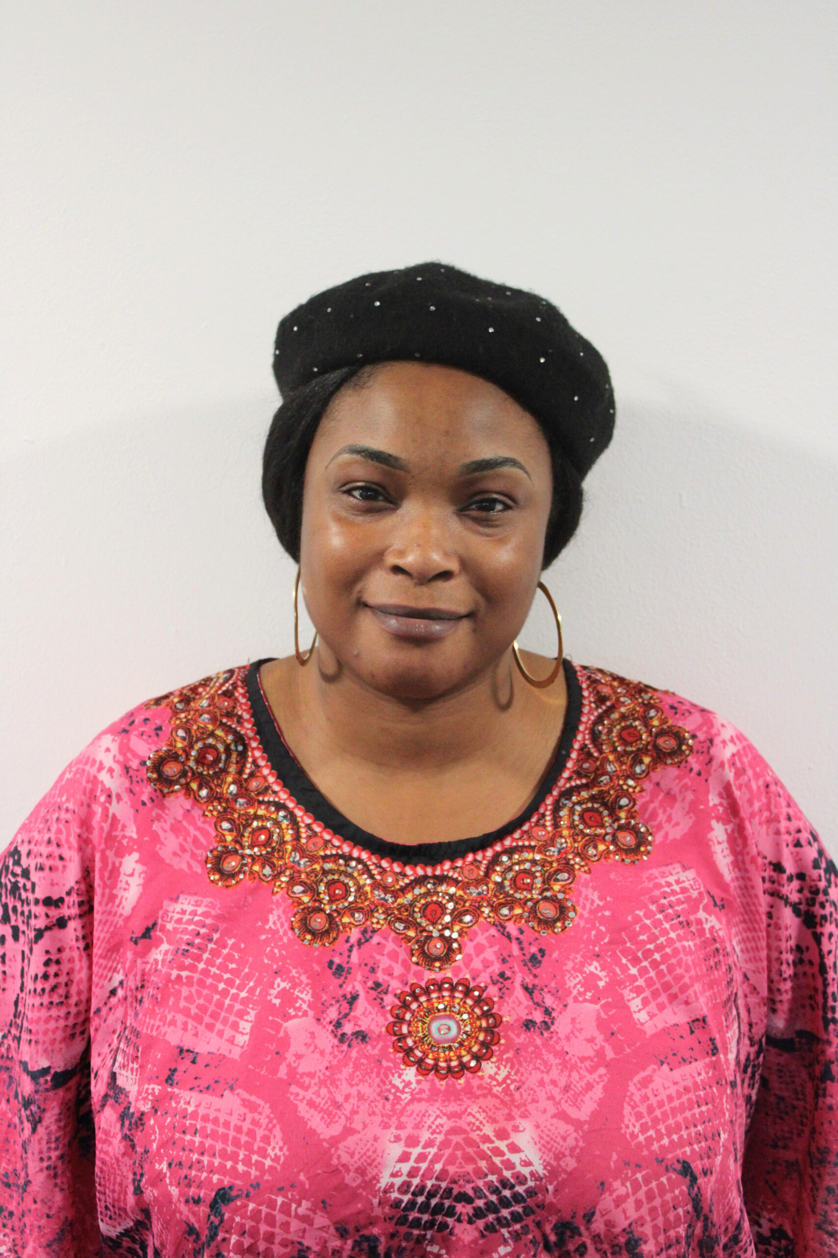 Headshot of Joyce, an Occupational Therapist at RSBC Dorton College. Joyce is a dark-skinned woman with dark-brown hair pulled back into a low bun. She is wearing a black beret with silver dots, a pink shirt with intricate designs and gold hoop earrings. She is looking straight at the camera and smiling softly.