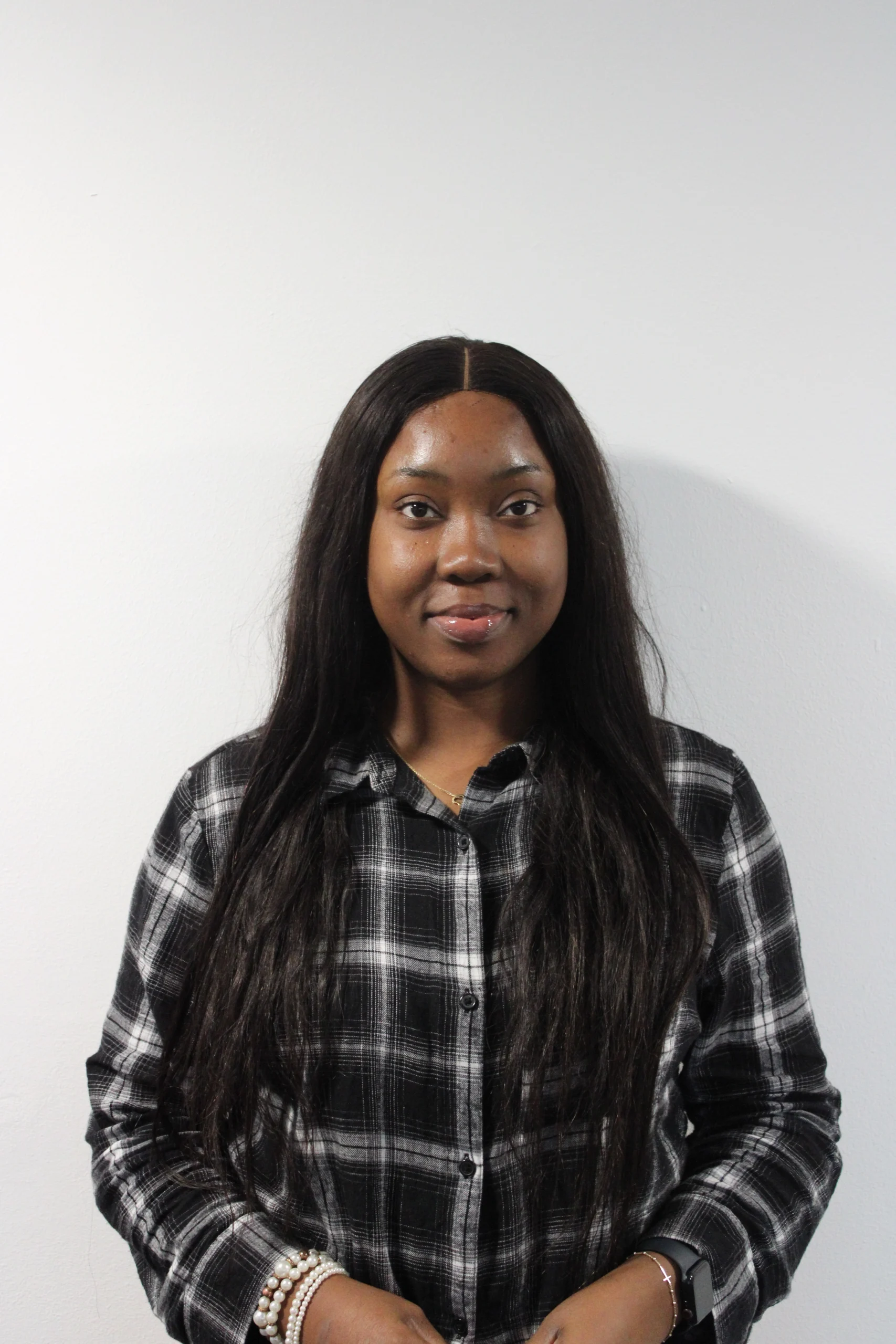 Juliet is a young dark skinned woman with long straight black hair. She is wearing a black and white tartan long sleeves shirt and is smiling softly at the camera.