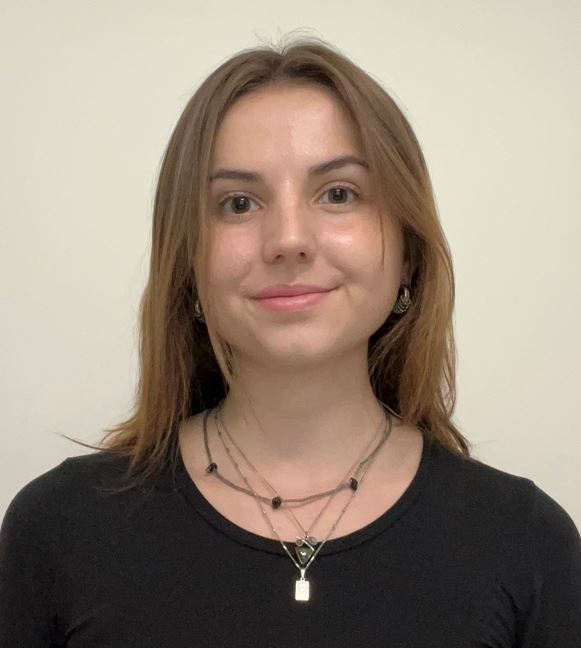 Laura is a light-skin young woman with light brown hair. She is wearing a black t-shirt and a few necklaces. She has brown eyes. She is looking directly at the camera and smiling.