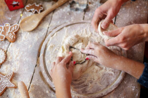 Family holiday activity. Top view of mother's and kid's hands making Christmas tree cookies on wooden table background.