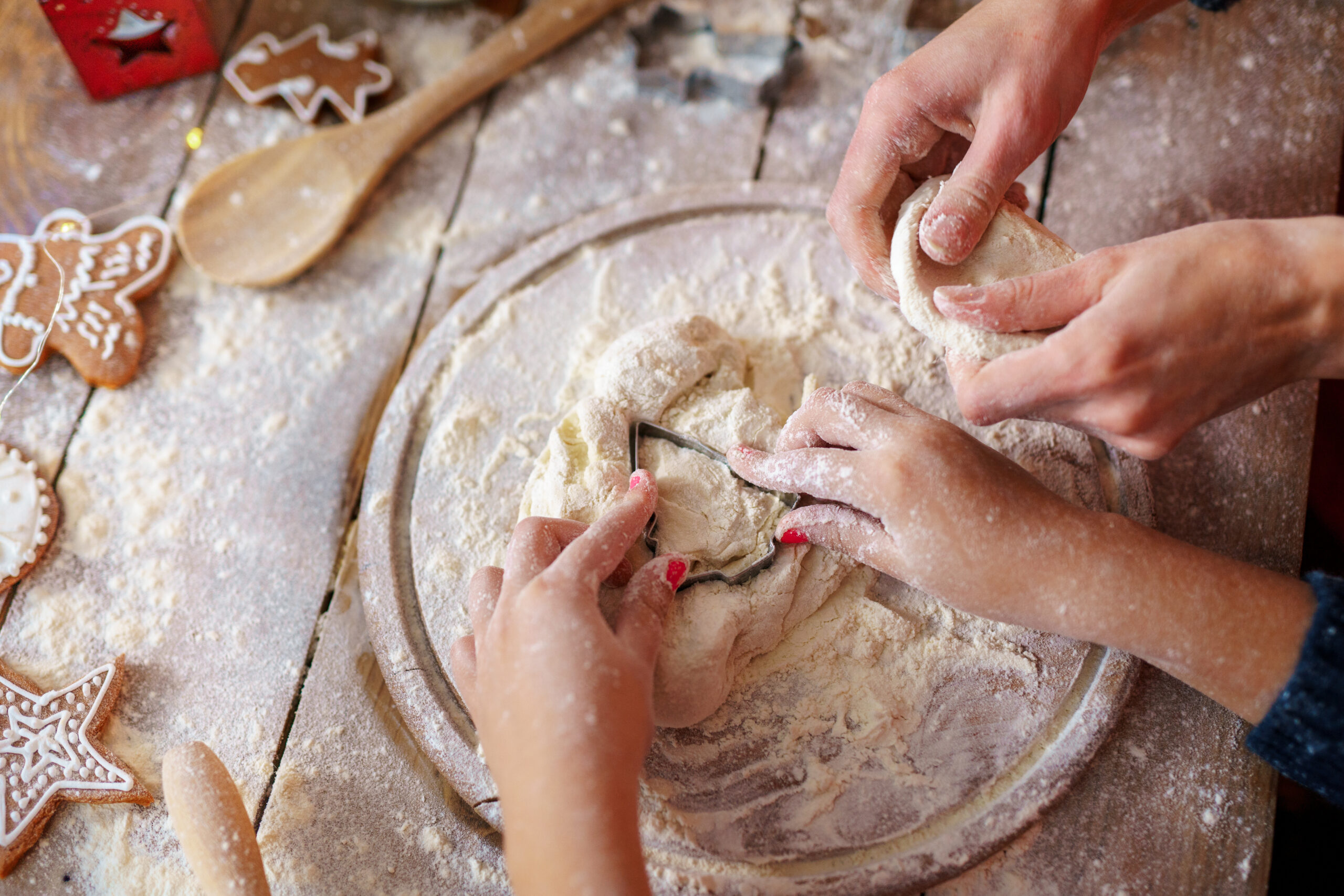 Family holiday activity. Top view of mother's and kid's hands making Christmas tree cookies on wooden table background.