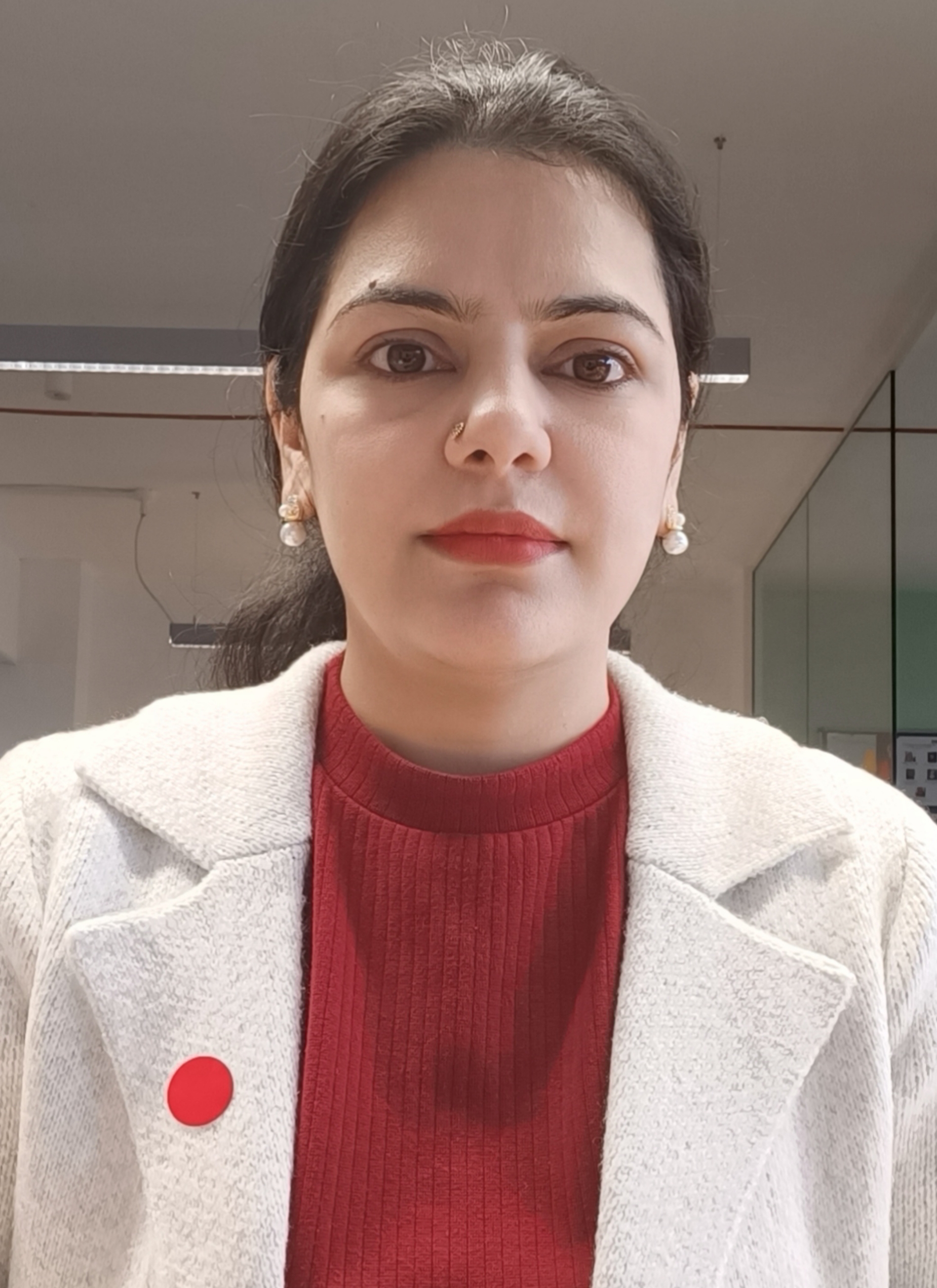 Huma, a Learning Support Assistant wearing a white blazer and dark orange high neck top. She has black hair and is wearing white pearl stud earrings.