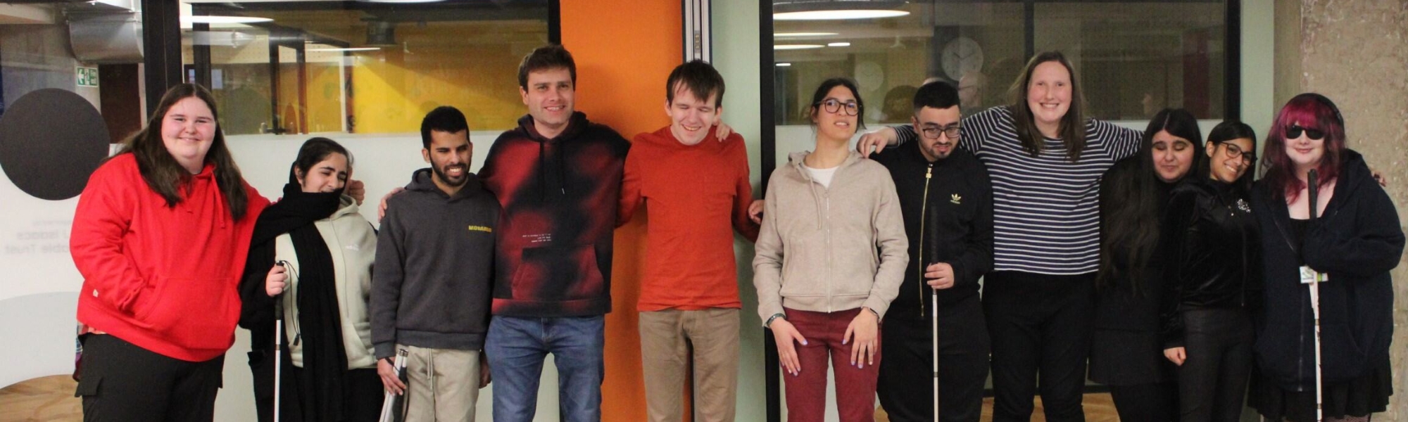 Members of the Youth Forum group and VI mentors in line against a wall. They are all smiling an posing for the camera creating a warm, friendly and dynamic atmosphere.