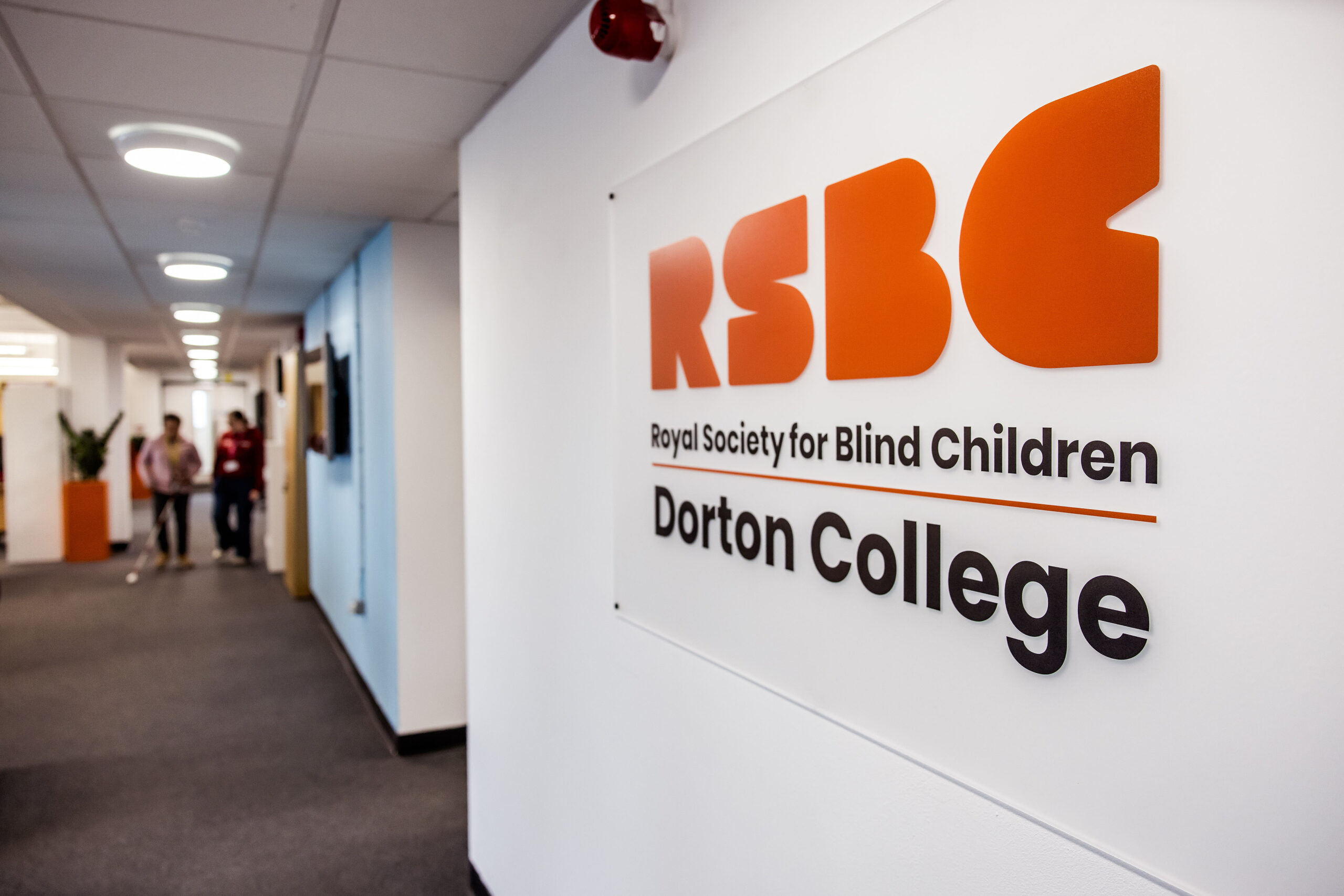 A photograph of the Royal Society for Blind Children Dorton College sign. The sign is on a wall to the right of where the camera is pointing. The camera is pointing down the Dorton College hallway.